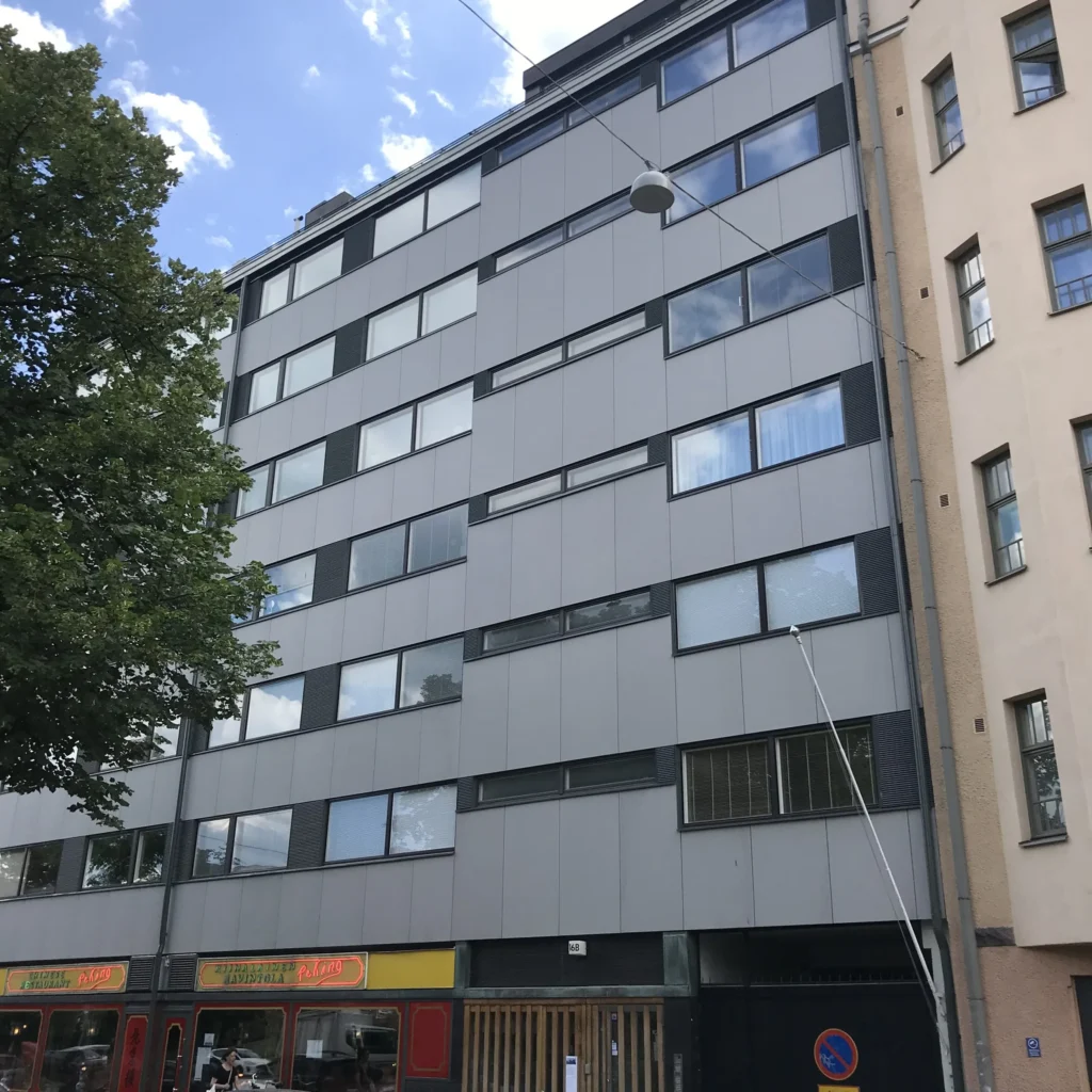 Aleksis Kiven kadun vaaleanharmaa concrete skin -kuitubetonijulkisivu ja tummanharmaat tehostepaneelit sinistä taivasta vasten, Helsinki