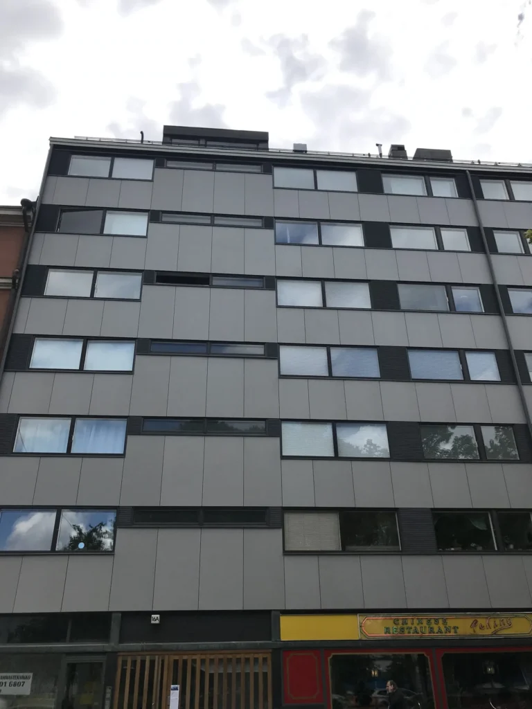 Aleksis Kiven kadun vaaleanharmaa concrete skin -julkisivu alaviistosta, tummat tehostepaneelit ja ikkunarivit, Helsinki