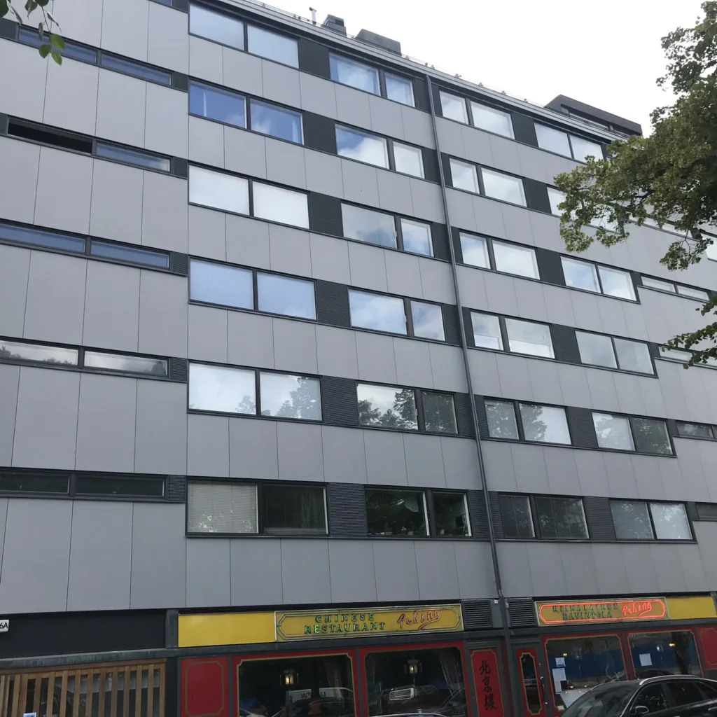 Aleksis Kiven kadun vaaleanharmaa concrete skin -kuitubetonijulkisivu ja tummat tehostepaneelit, katutasossa kiinalainen ravintola, Helsinki