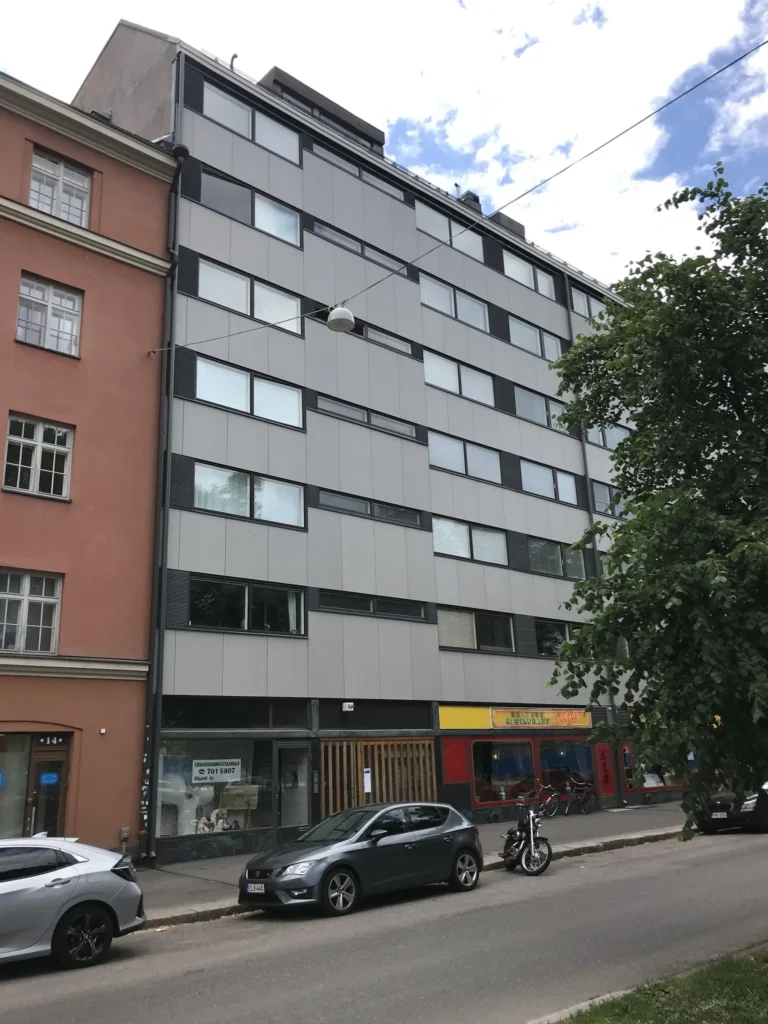 Aleksis Kiven kadun concrete skin -kuitubetonijulkisivu kadulta kuvattuna, etualalla pysäköityjä autoja, Helsinki