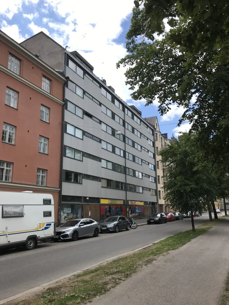 Aleksis Kiven kadun vaaleanharmaa concrete skin -julkisivu vanhempien rapattujen rakennusten välissä katunäkymässä, Helsinki