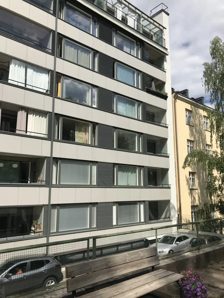 Aleksis Kiven kadun sisäpihan vaalea concrete skin -julkisivu ja lasitetut parvekkeet, etualalla penkki, Helsinki