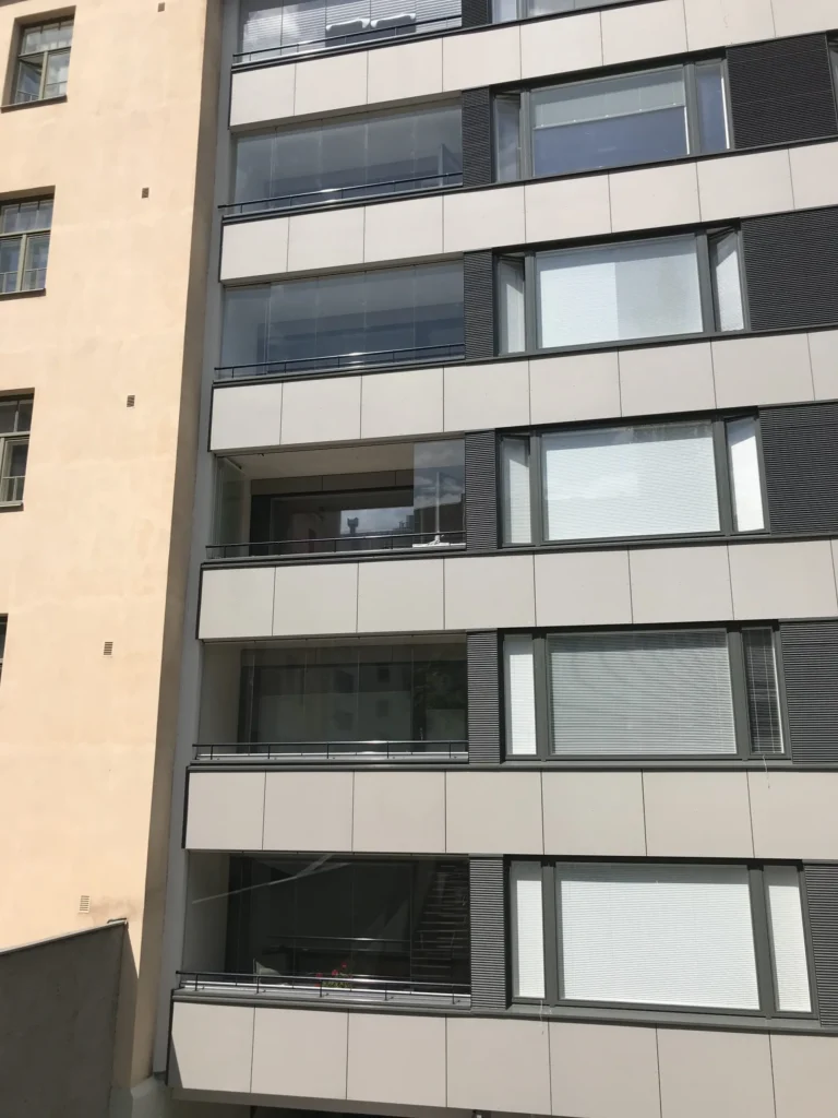 Aleksis Kiven kadun sisäpihan lasitetut parvekkeet ja vaaleat concrete skin -levyt vanhemman rakennuksen vieressä, Helsinki
