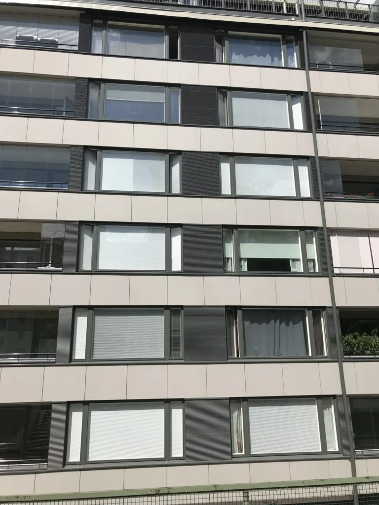 Lähikuva Aleksis Kiven kadun sisäpihan lasitetuista parvekkeista ja vaaleista concrete skin -levyistä, Helsinki