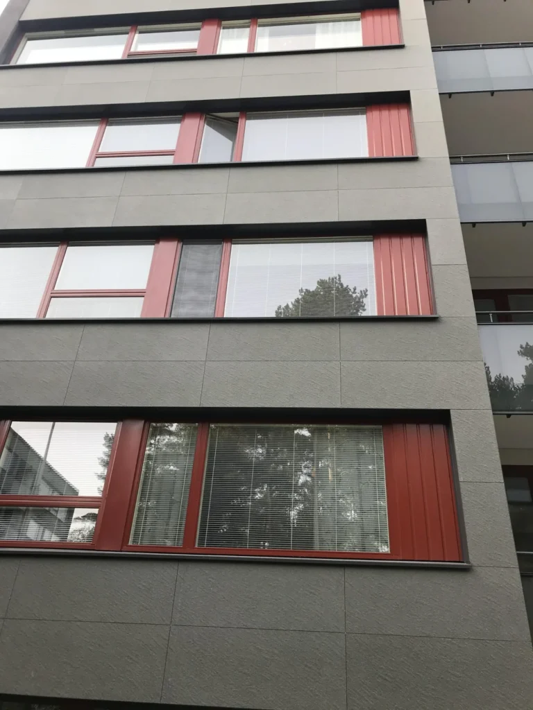 Lähikuva As Oy Nunnanhaan ikkunalinjasta, punaisista ikkunapuitteista ja harmaasta julkisivulevytyksestä
