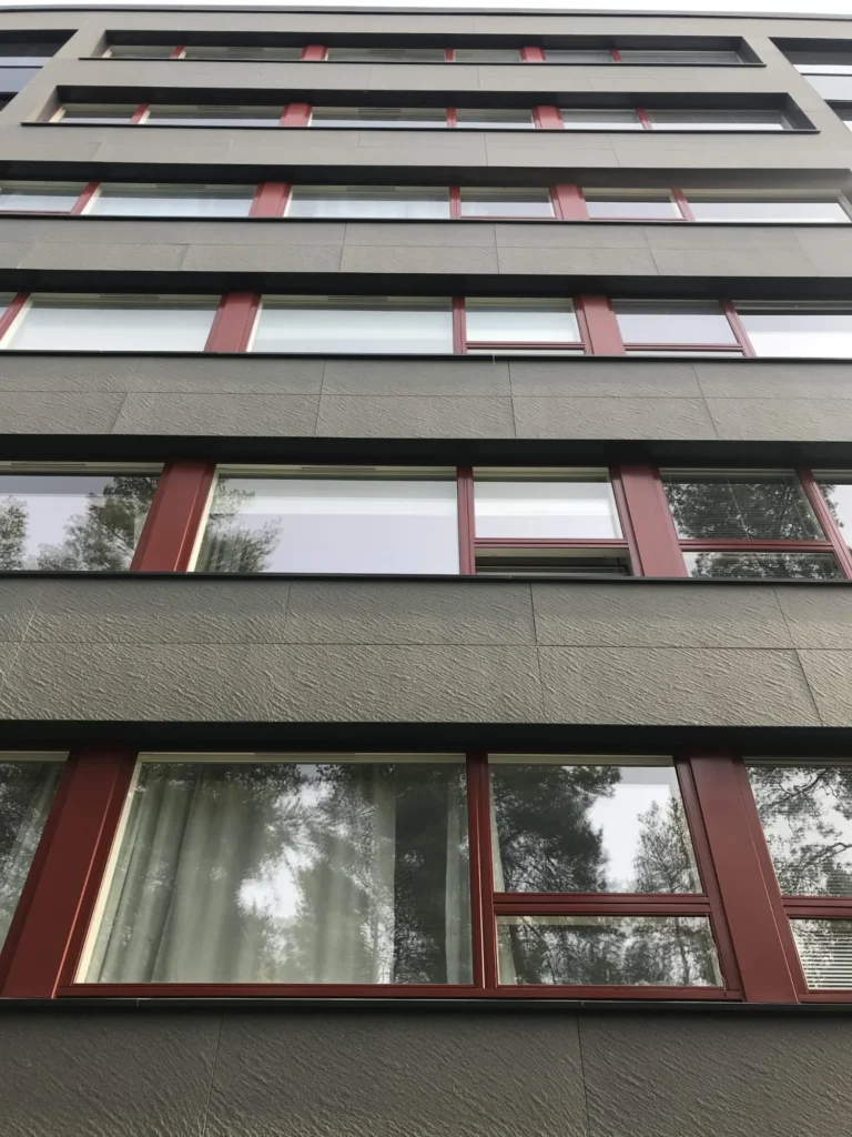 Alhaalta kuvattu As Oy Nunnanhaan julkisivu, punaiset ikkunapuitteet ja harmaa levyverhous