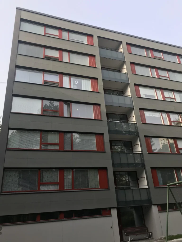 As Oy Nunnanhaan harmaa julkisivu punaisilla ikkunapuitteilla ja keskellä lasitetut parvekelinjat