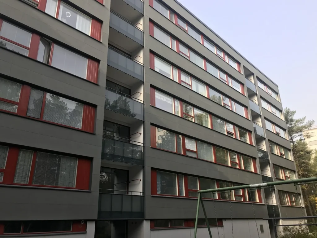 As Oy Nunnanhaka julkisivu ja leikkipiha, harmaa levyverhous, punaiset ikkunapuitteet ja lasitetut parvekkeet