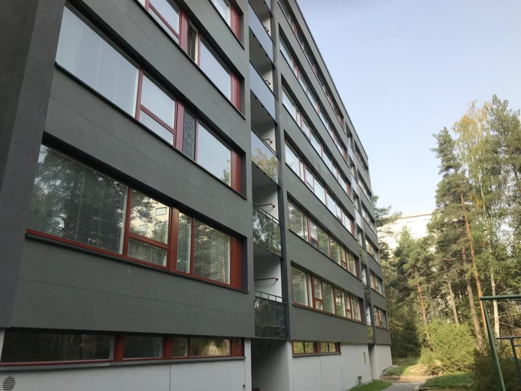 As Oy Nunnanhaka rakennuksen sivujulkisivu, punaiset ikkunat, harmaat levyt ja metsäinen ympäristö