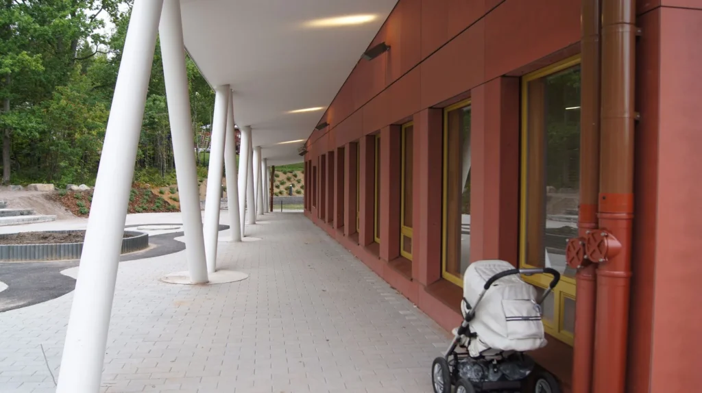 Auroran koulun terrakotanpunainen concrete skin -kuitubetonijulkisivu ja katettu kulkuväylä valkoisine vinopilareineen, Espoo