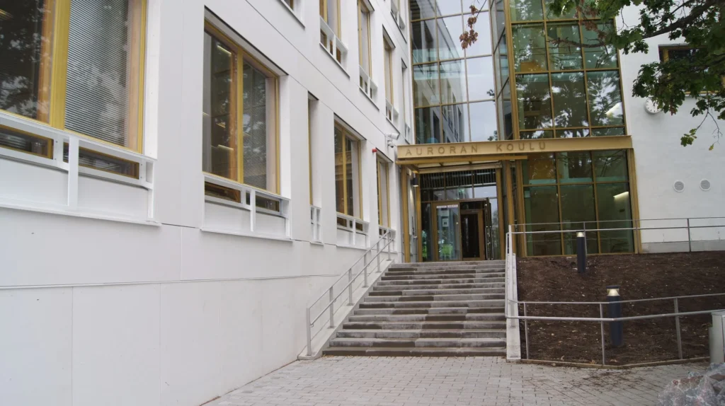 Auroran koulun pääsisäänkäynti ja valkoinen öko skin -julkisivu, sisäänkäynnin yllä kultainen Auroran koulu -teksti, Espoo