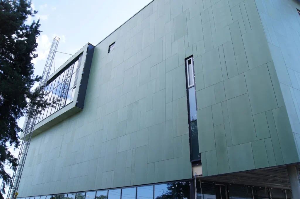 Herttoniemen metrovalvomon vihreä concrete skin -julkisivu alaviistosta, ulokkeellinen lasikuutio ja kapea ikkuna, Helsinki
