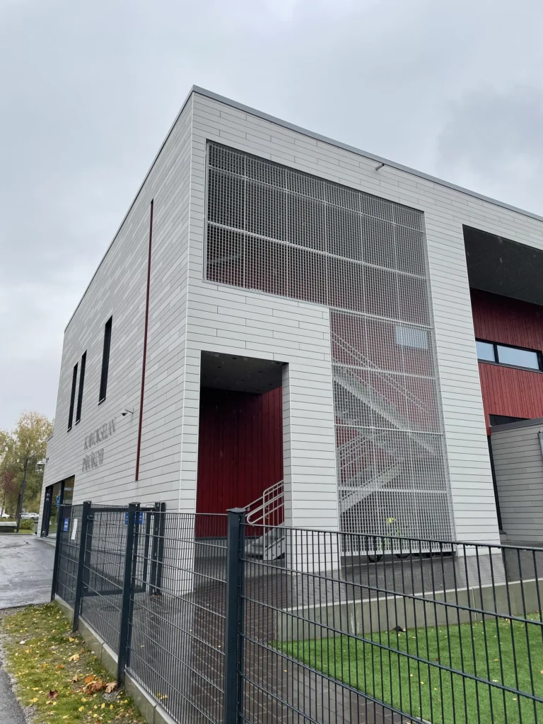 Kaivokselan koulun harmaa öko skin -julkisivu, teräsverkkoporras ja punainen sisäänkäyntisyvennys, Vantaa