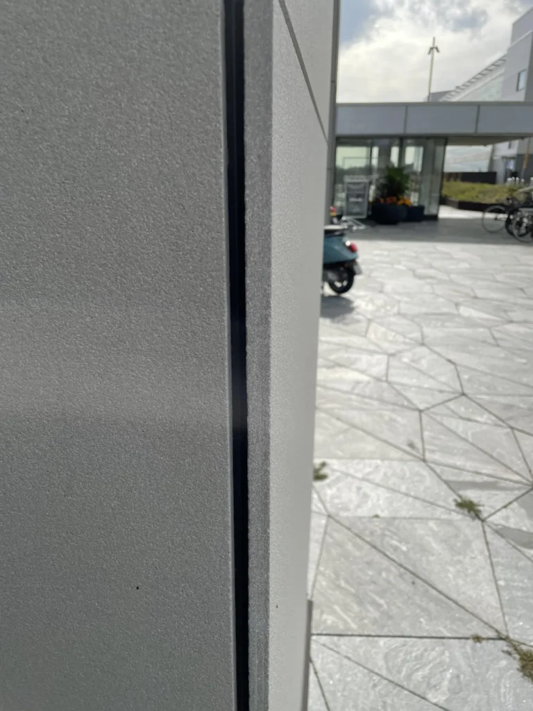 Keilaniemi A-tornin vaaleanharmaa concrete skin -kuitubetonijulkisivu lähikuvassa, taustalla aukio ja sisäänkäynti, Espoo