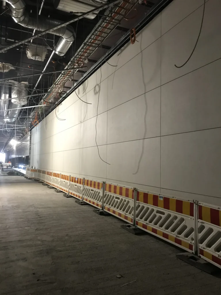 Kivenlahden metron pitka concrete skin -seina laituritasolla, tyomaa-aidat ja paljas tekniikkakatto, Espoo
