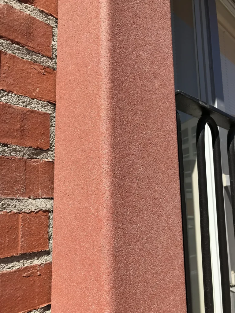 As Oy Koirasaarentie 36:n korallinpunainen concrete skin -pinta ikkunan pielessa tiilimuurin vieressa, Helsinki