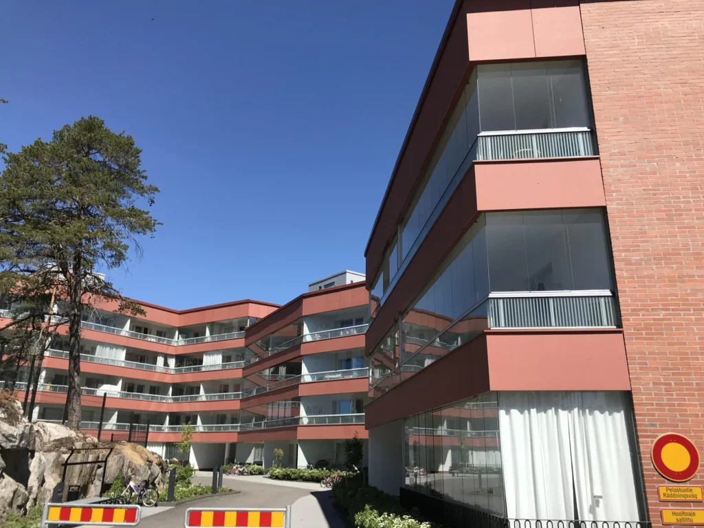 As Oy Koirasaarentie 36:n kaartuva korallinpunainen concrete skin -pihajulkisivu ja tiilipaaty, Helsinki