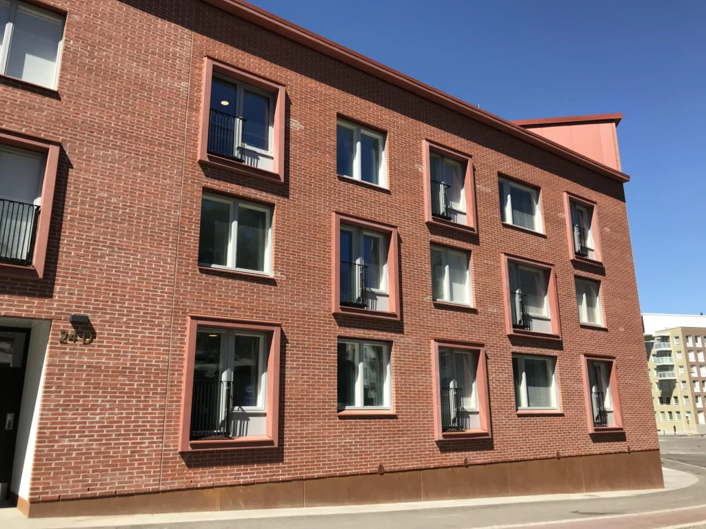 As Oy Koirasaarentie 36:n punatiilinen julkisivu, jossa korallinpunaiset concrete skin -ikkunapielet, Helsinki