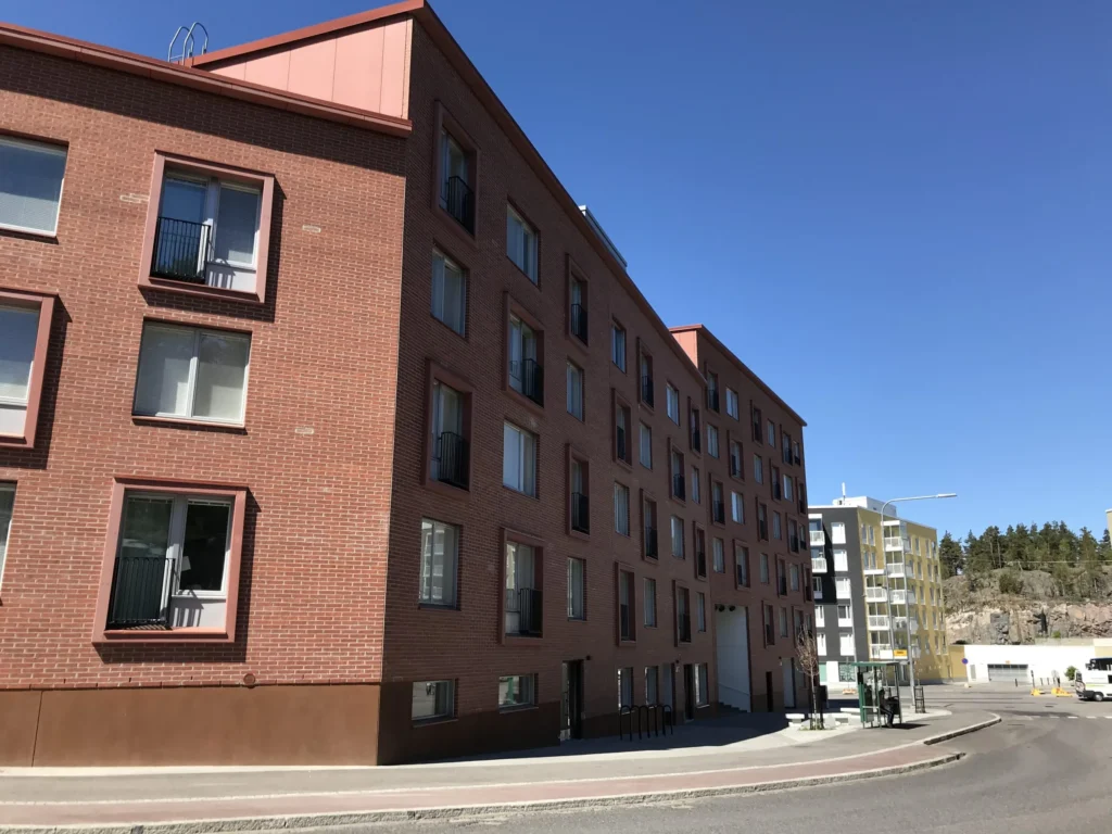 As Oy Koirasaarentie 36:n punatiilinen julkisivu concrete skin -detaljein kadunkulmassa, Helsinki