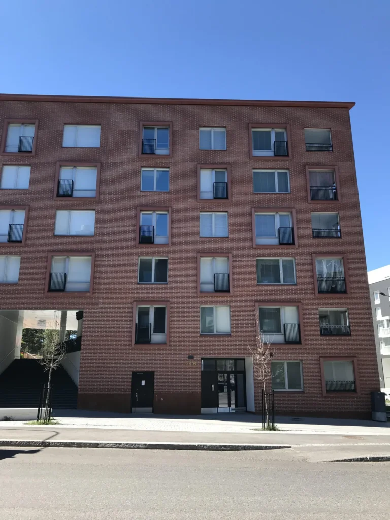 As Oy Koirasaarentie 36:n punatiilinen paatyjulkisivu sisaankaynteineen ja concrete skin -pielineen, Helsinki