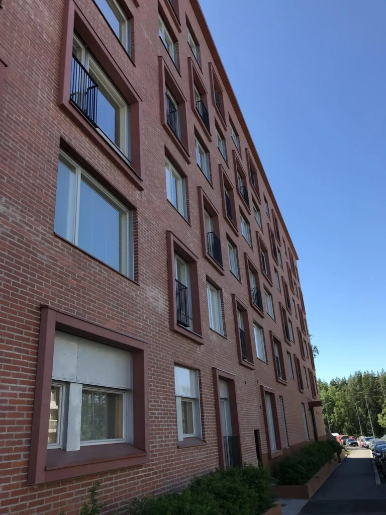 As Oy Koirasaarentie 36:n pitka punatiilinen julkisivu concrete skin -ikkunapielineen alaviistosta kuvattuna, Helsinki