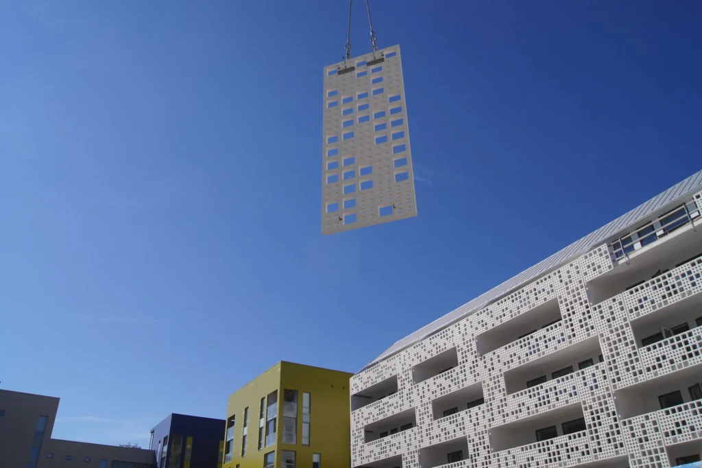 Valkoinen cast 3D -pitsielementti nosturin varassa sinistä taivasta vasten valmiin julkisivun yläpuolella, Länsisatamankatu 23