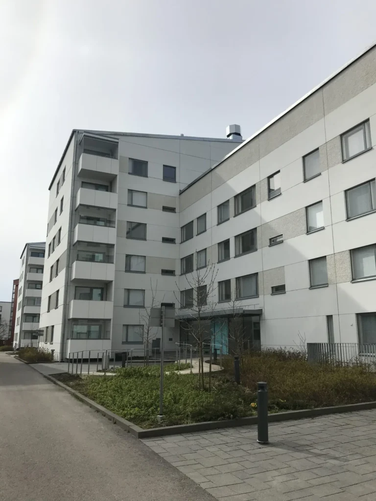 Korttelinäkymä Luutnantinpolku 2:n asuinkerrostalosta, jossa vaaleat Concrete Skin -levyt täydentävät rakennuksen julkisivua