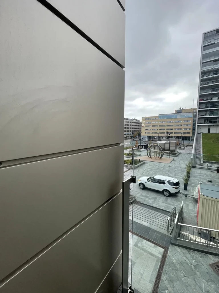 Lähikuva julkisivulevyn saumasta ja näkymästä Mall of Triplan pihatasolle harmaan sään valossa