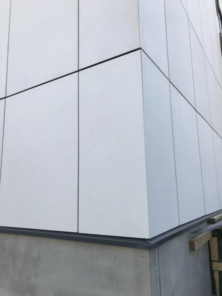 Syöpäklinikan vaalea kuitubetonipinta ja pystysauma julkisivun lähikuvassa